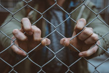 Image of hands holding prison fence